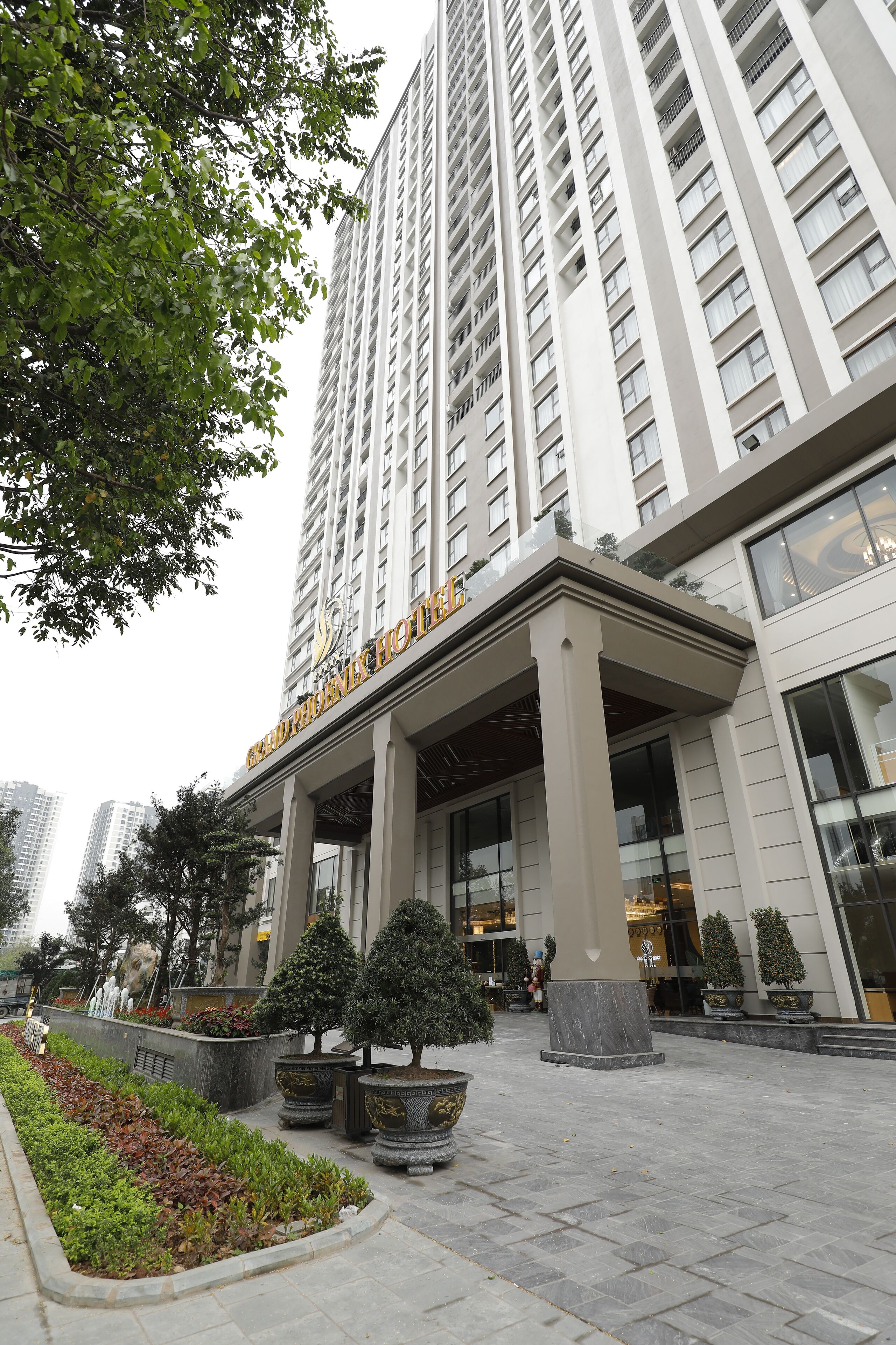 A hotel entrance with a modern facade, large windows, and a well-maintained garden area with potted plants.