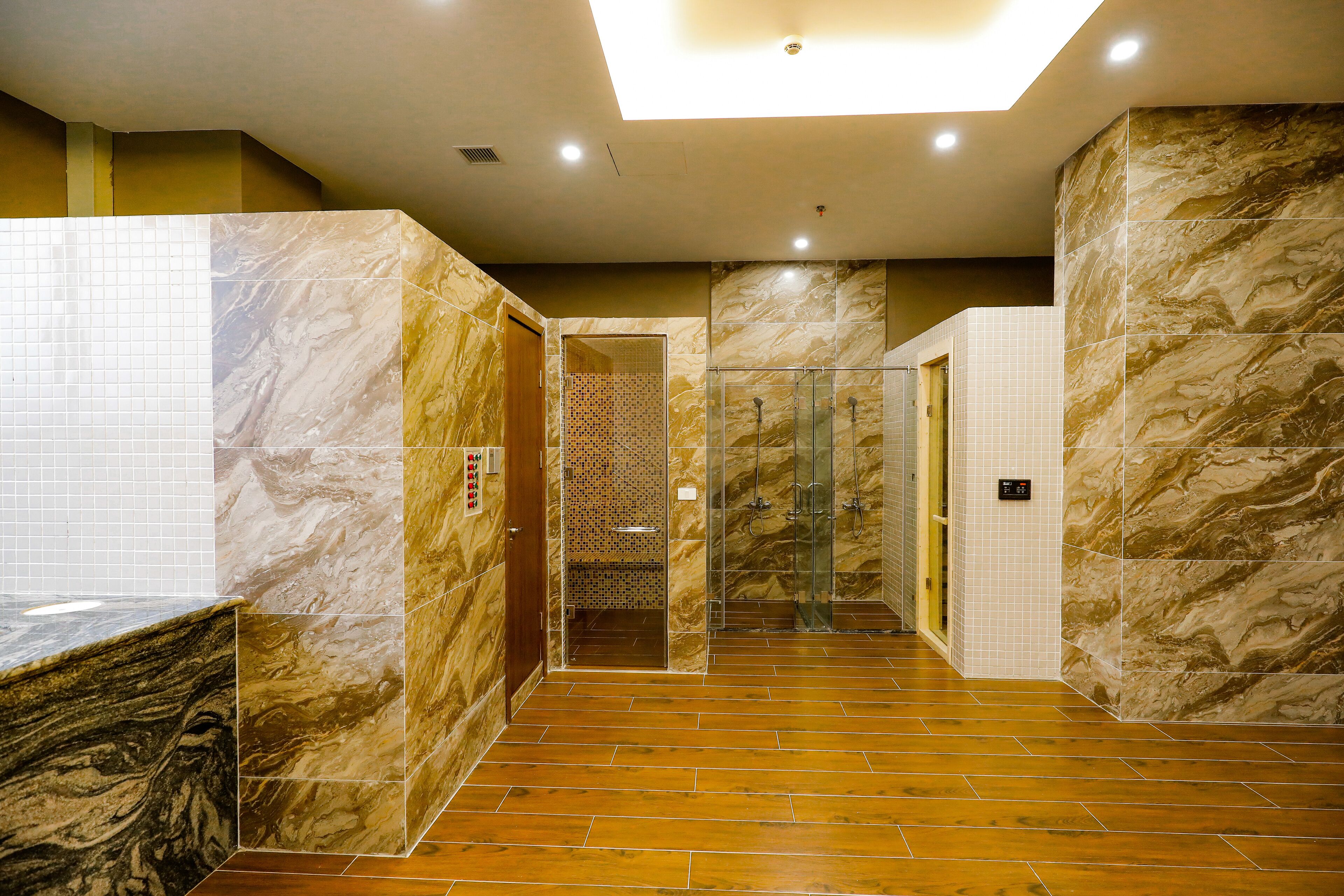 Un baño moderno con paredes de mármol, cabina de ducha con mampara de vidrio y suelo de madera.