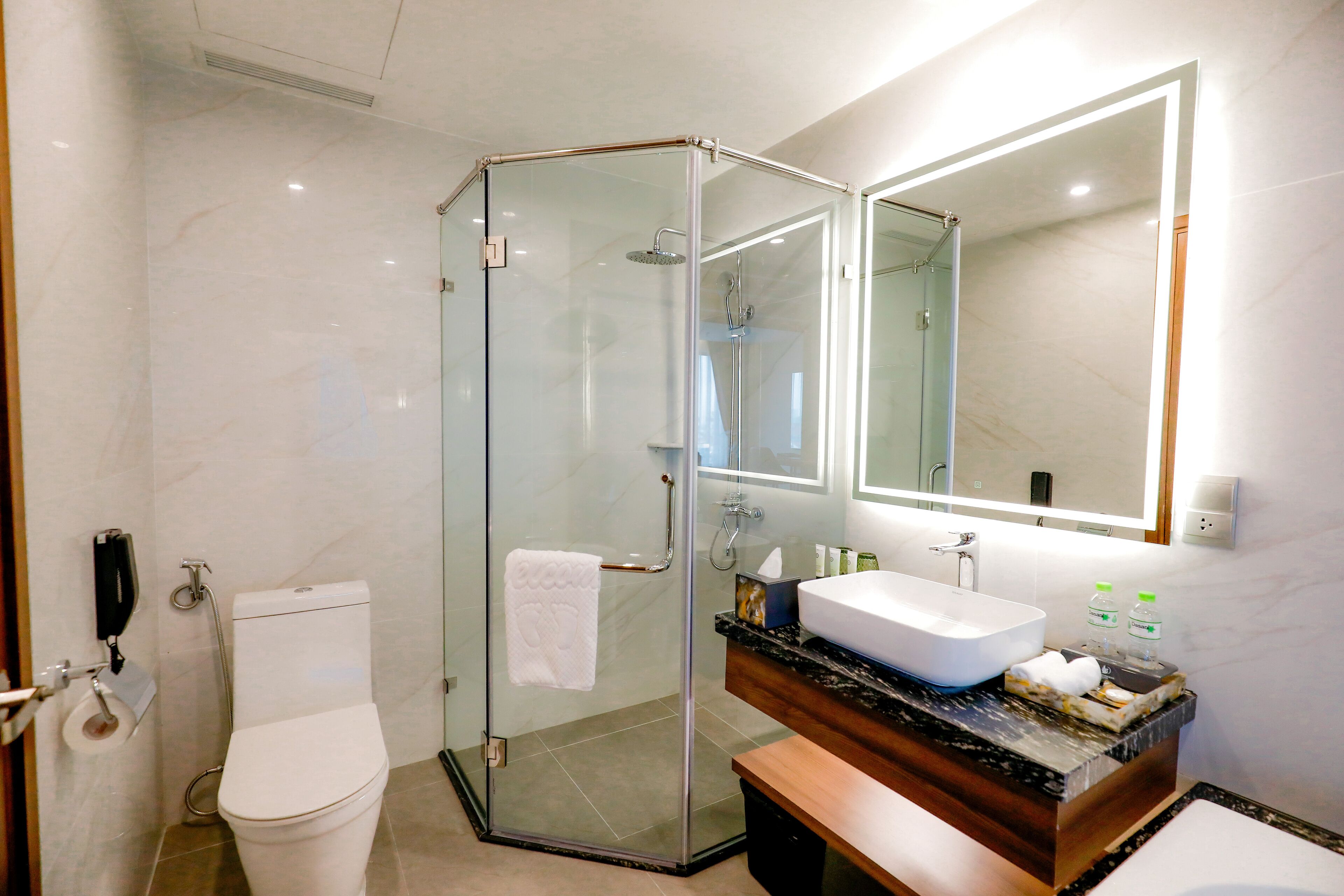 Ein modernes Badezimmer mit einer gläsernen Duschkabine, einer weißen Toilette, einem Waschbecken mit Holzschublade und einem großen Spiegel.