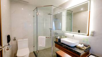 Ein modernes Badezimmer mit einer gläsernen Duschkabine, einer weißen Toilette, einem Waschbecken mit Holzschublade und einem großen Spiegel.