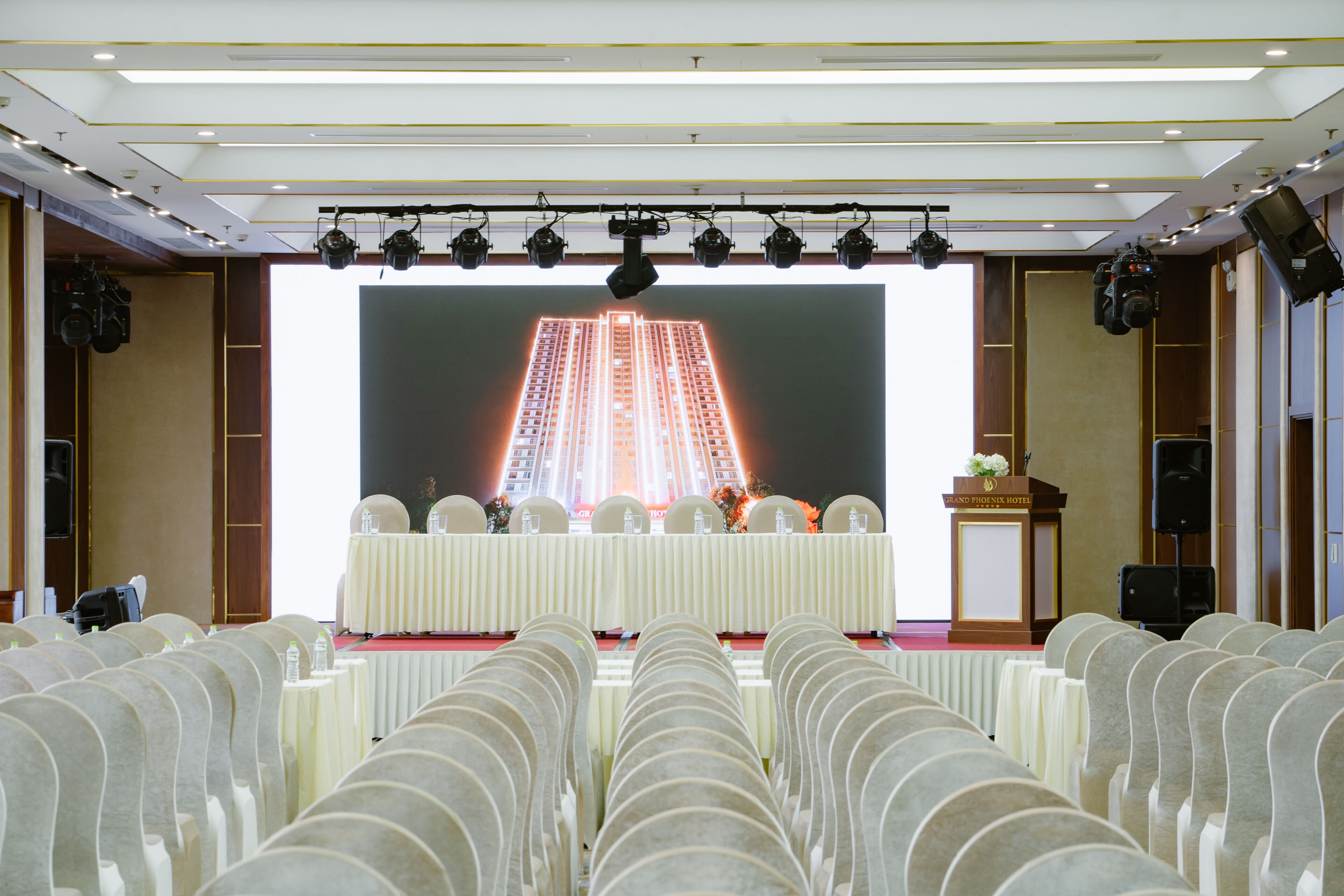 Ein Konferenzraum mit Reihen von Stühlen, die auf eine Bühne zeigen, auf der ein großer Bildschirm ein Gebäude zeigt.