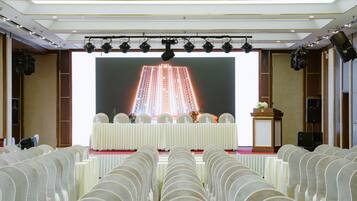Ein Konferenzraum mit Reihen von Stühlen, die auf eine Bühne zeigen, auf der ein großer Bildschirm ein Gebäude zeigt.