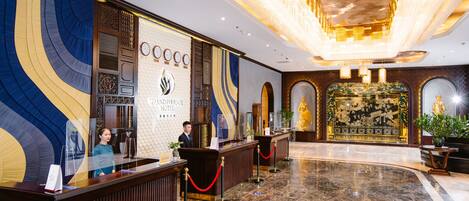 A hotel reception area with a marble floor, a reception desk, and a large chandelier.