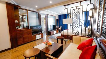 Habitación de hotel moderna con suelo de madera, un sofá con cojines rojos, un televisor, un escritorio y un espejo grande.
