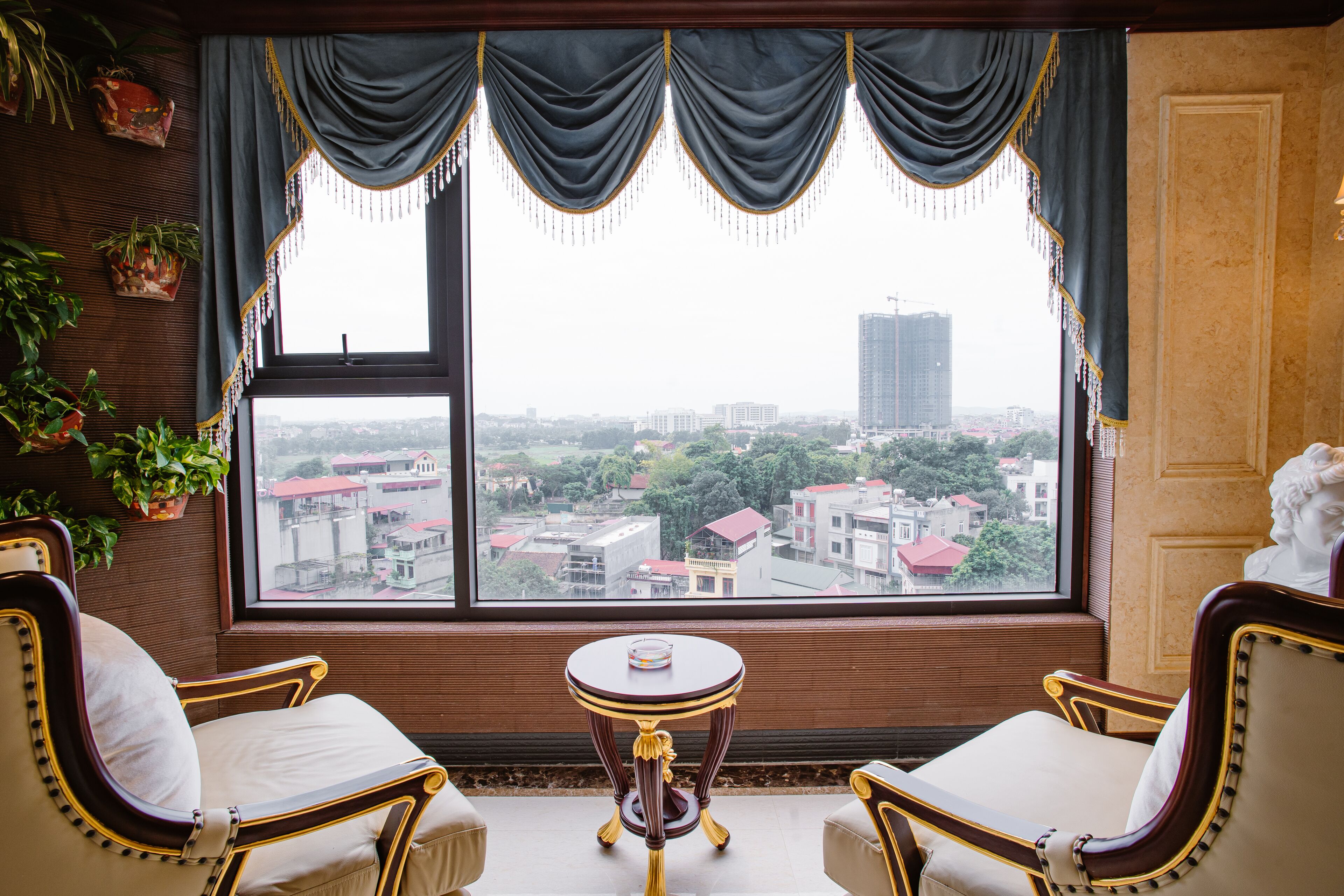 A room with a large window, two chairs, a small table, and decorative plants.