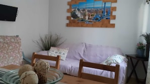 Een woonkamer met een bank, een bijzettafeltje met ijs en een televisie aan de muur, plus een schilderij.