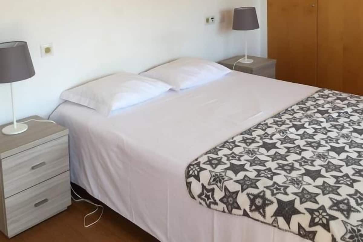 Un dormitorio con una cama, dos mesitas de noche, una lámpara, un armario y una lámpara colgante.