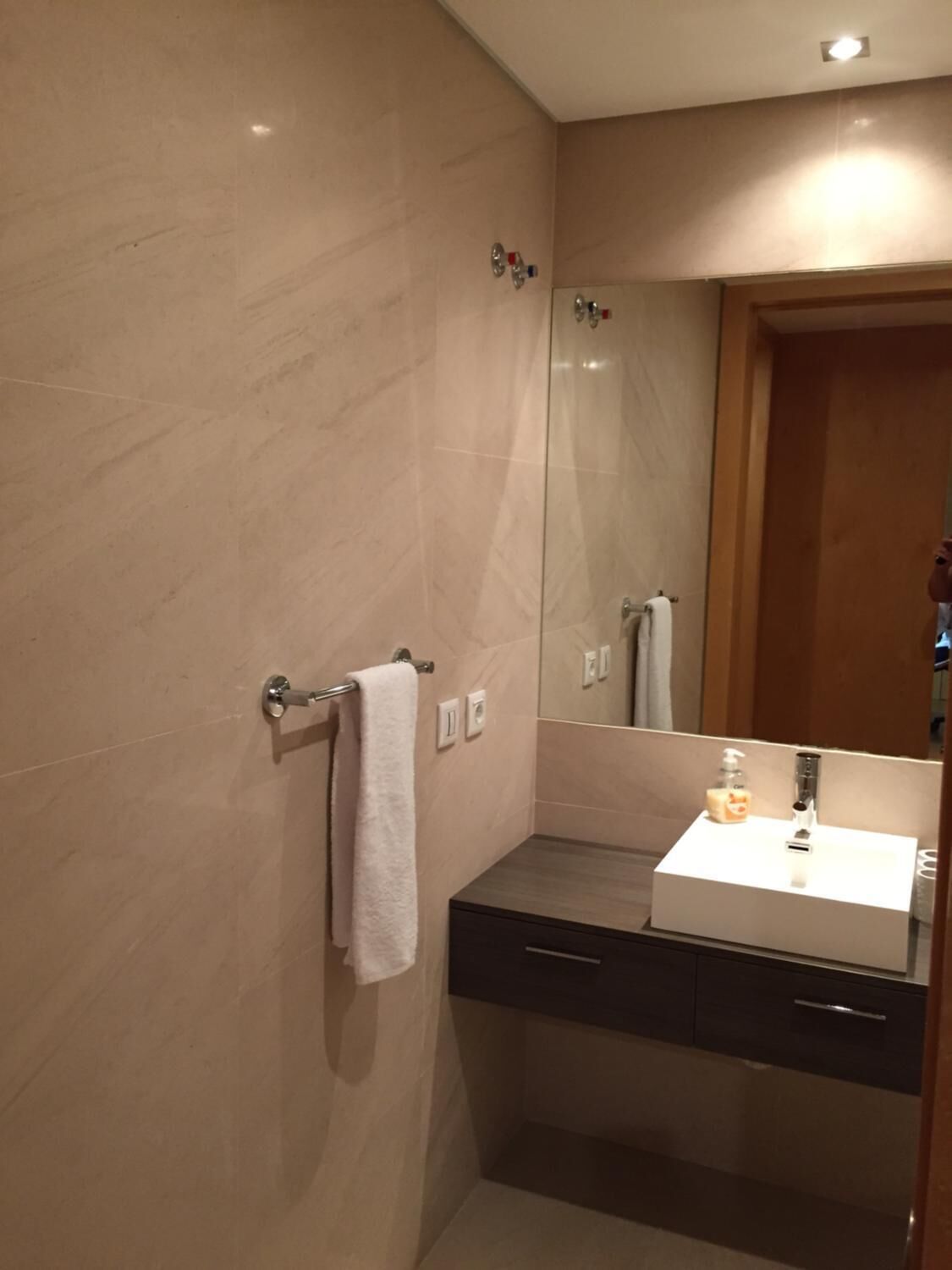 Une salle de bain moderne avec un grand miroir, un lavabo blanc et un porte-serviettes.