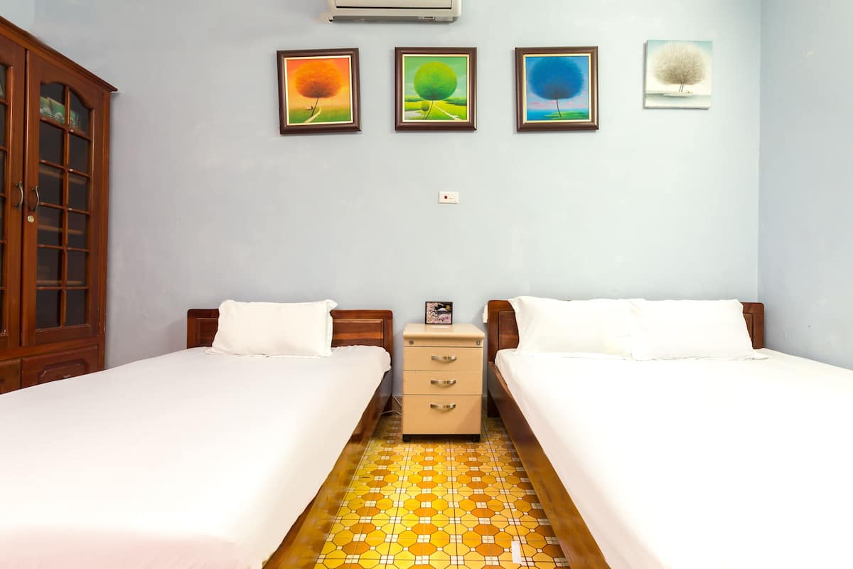 A room with two beds, a wooden wardrobe, a small bedside table, and a wall with four framed pictures.