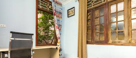 Una habitación con escritorio, silla de oficina y ventana con cortinas.