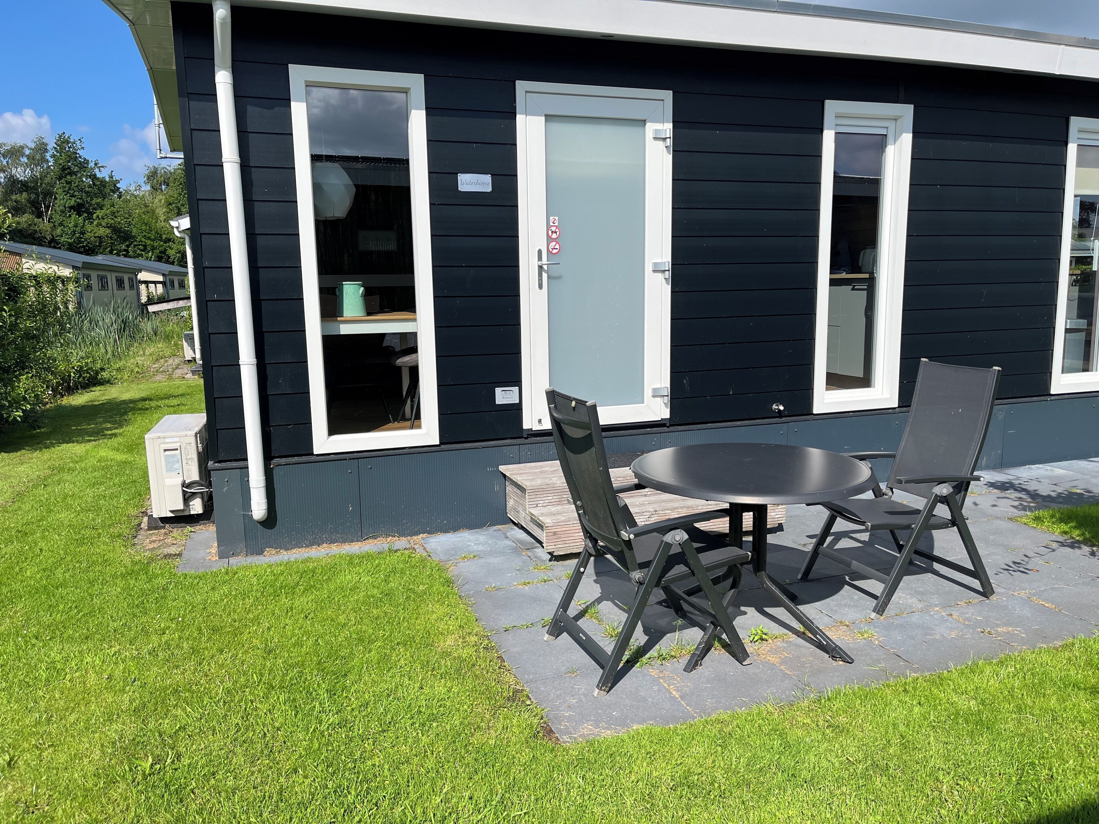 Una casa negra con detalles blancos, un pequeño patio con una mesa y sillas, y un letrero que dice "Welleskopia".