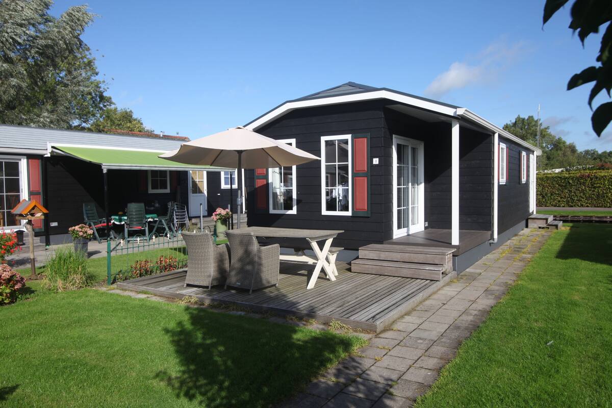 Una casa negra con contraventanas rojas, una terraza de madera y una mesa con sillas.