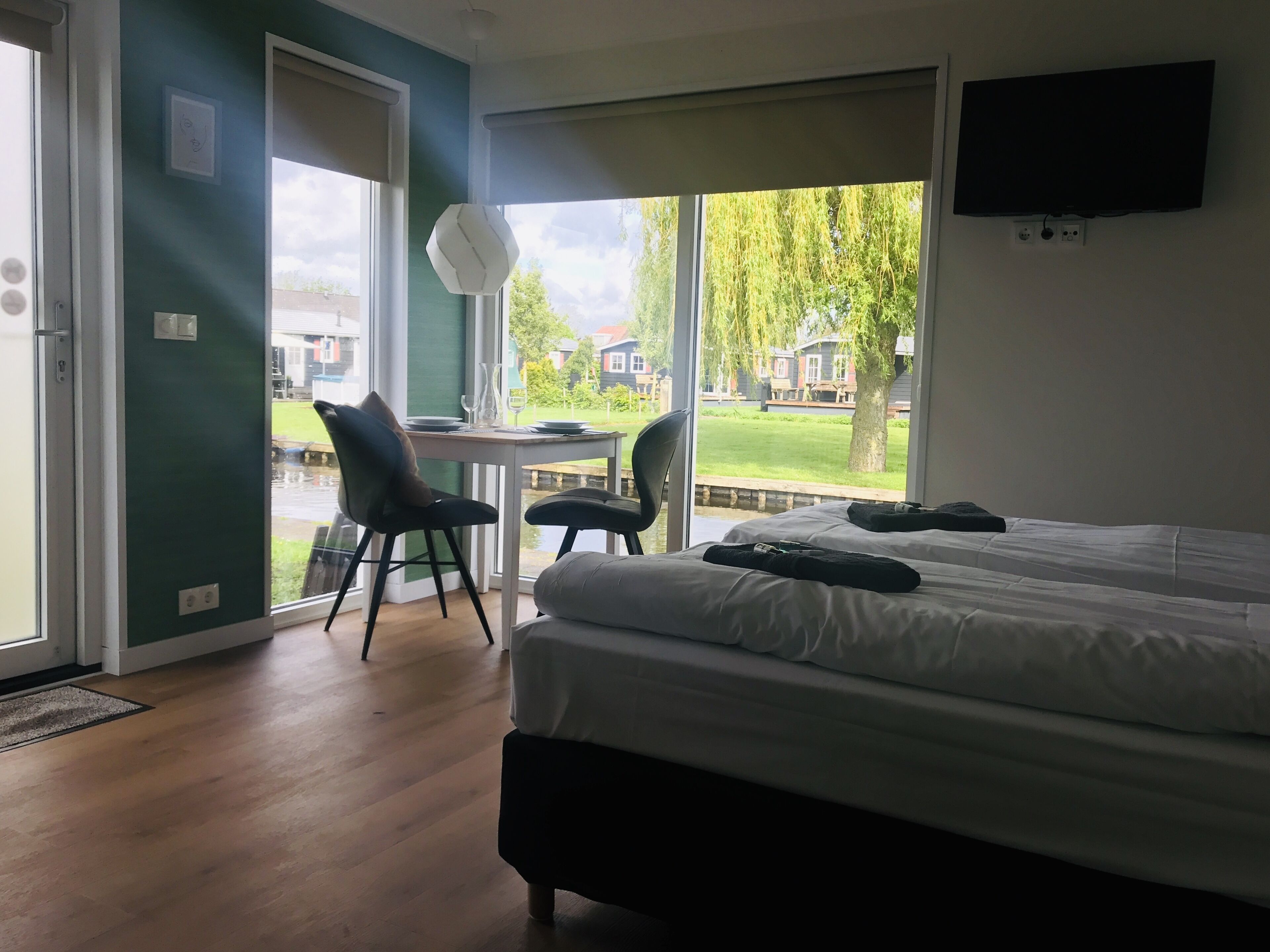 Ein Schlafzimmer mit einem Bett, zwei Stühlen, einem Tisch mit einer Vase und einem Fernseher an der Wand.