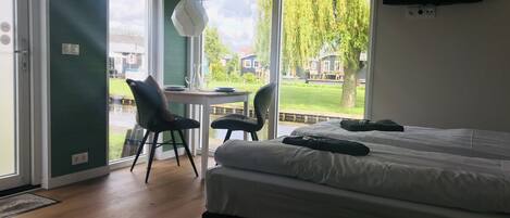 Un dormitorio con una cama, dos sillas, una mesa con un florero y un televisor en la pared.