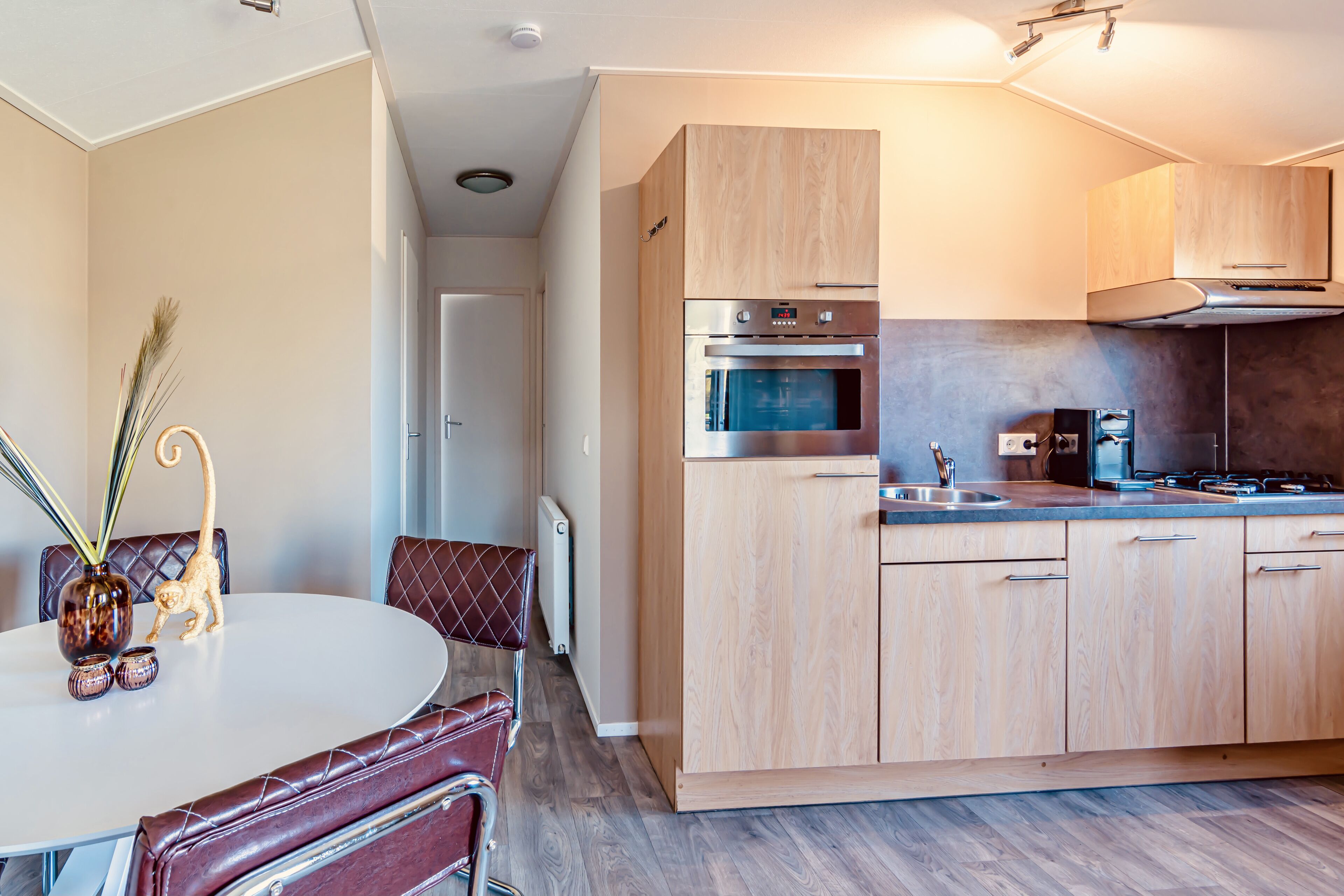 Een moderne keuken met houten kastjes, roestvrijstalen apparatuur en een eethoek met een ronde tafel en leren stoelen.