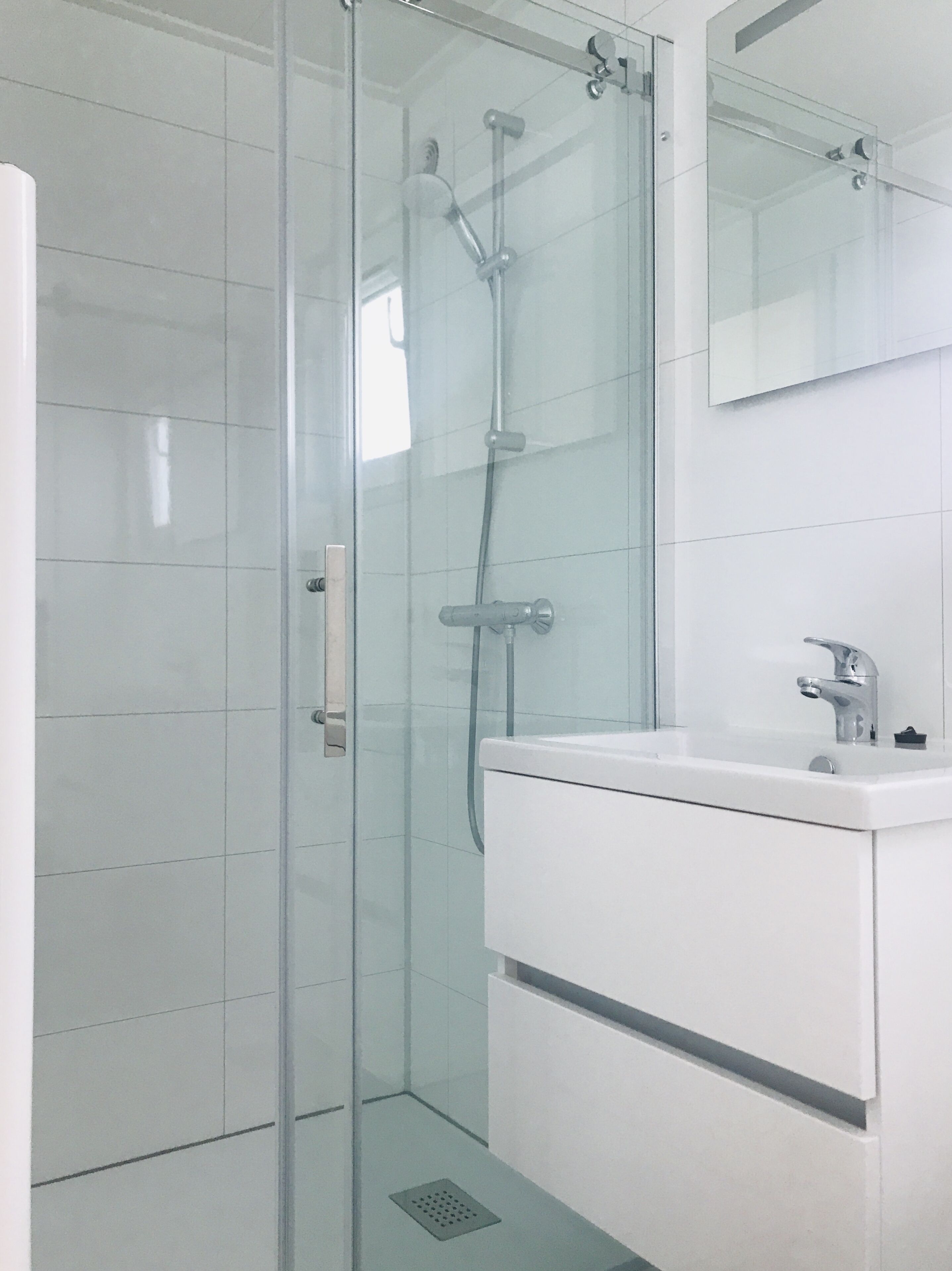 Ein modernes Badezimmer mit einer Duschkabine aus Glas, einem weißen Waschbecken und einem Spiegel darüber.