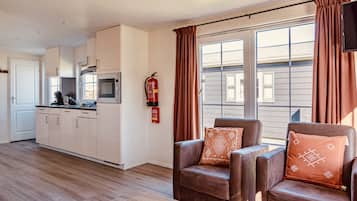 Une cuisine moderne avec des meubles blancs, un four à micro-ondes et une cuisinière. On y trouve deux fauteuils en cuir marron avec des coussins à motifs. Un extincteur est fixé au mur.