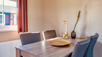 Un coin repas comprenant une table en bois, quatre chaises, une assiette décorative, un vase avec des plantes et une fenêtre avec des rideaux.