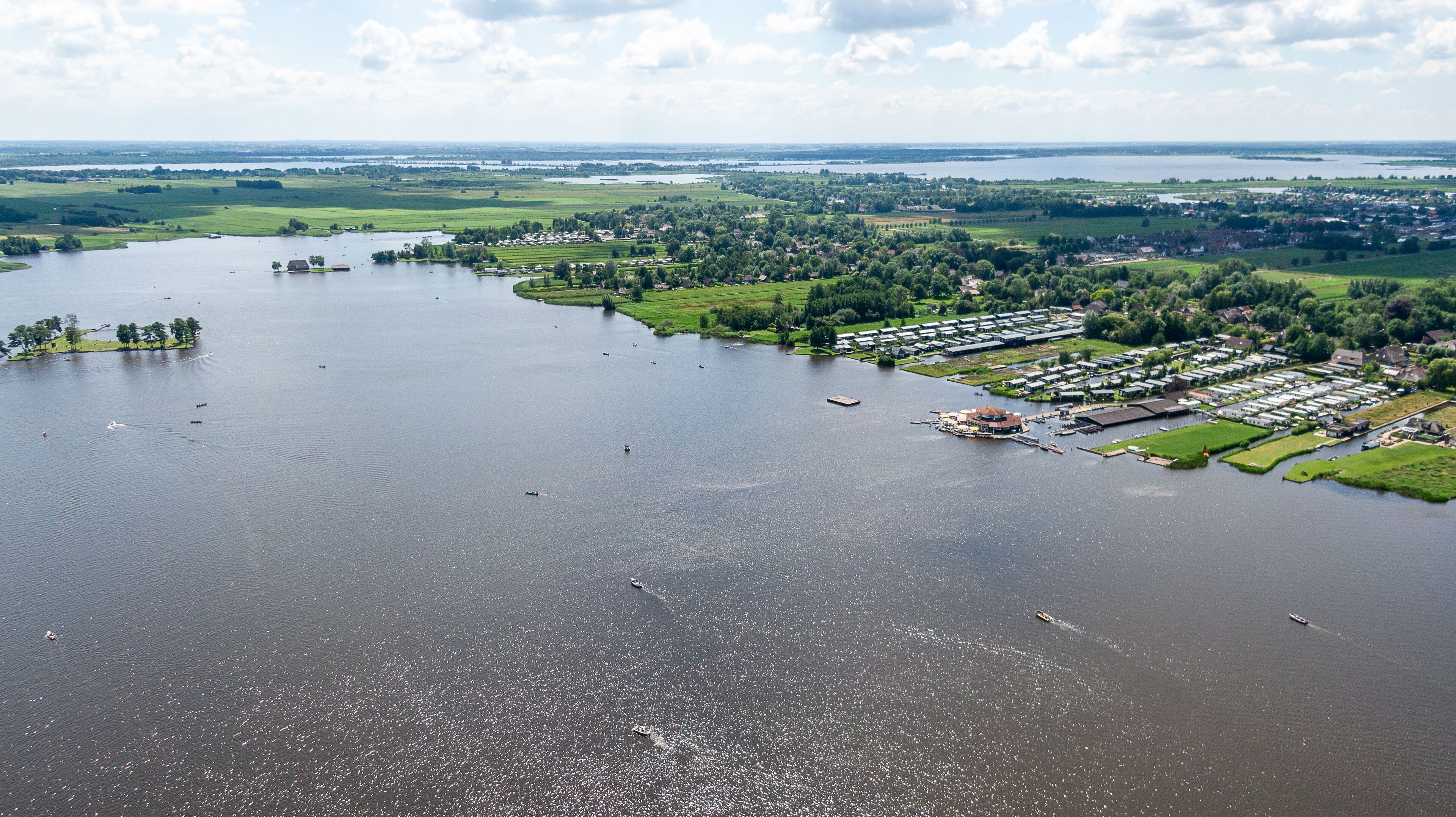 An aerial view of a riverside area with a marina, green fields, and residential buildings.