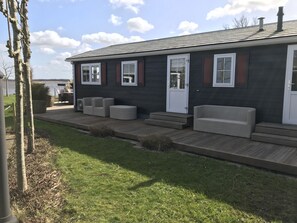 A modern house with a dark exterior, a front porch with outdoor furniture, and a view of a lake. - Kroondomein Giethoorn (Giethoorn)