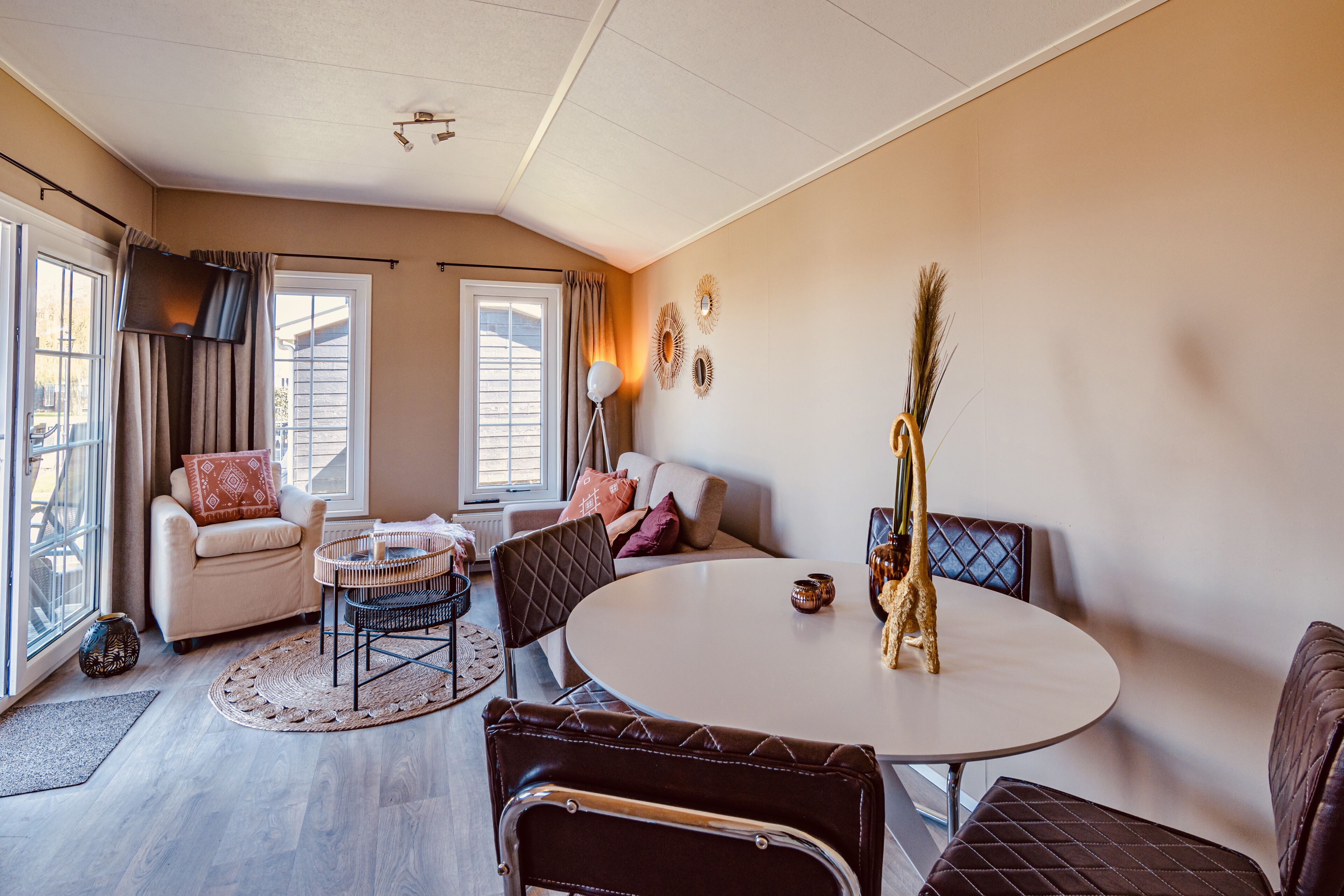 A modern living room with a round table, leather chairs, a sofa, and a large window.