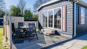A small wooden cabin with a deck, a table, and chairs.