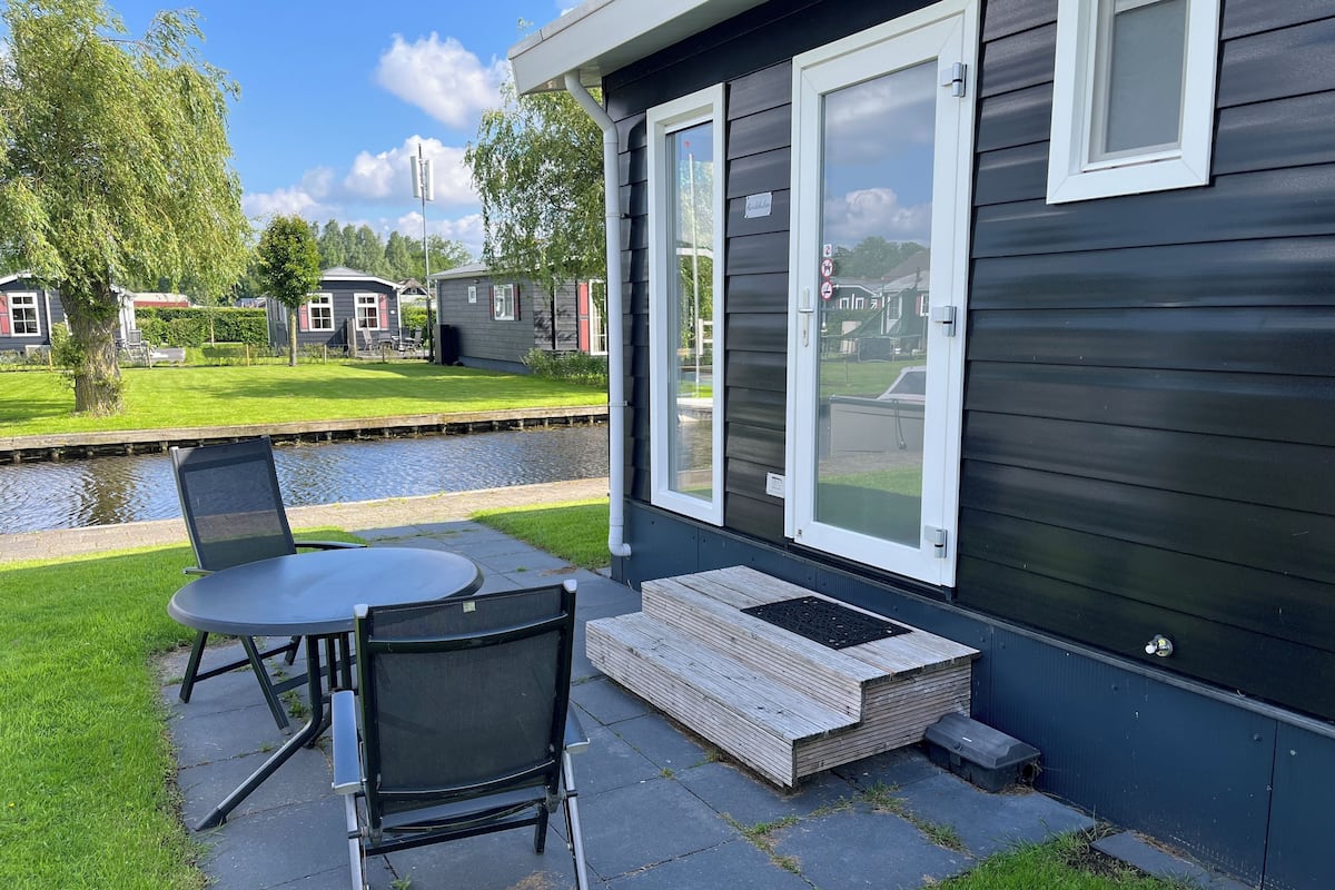 Un patio con mesa y sillas, una pequeña terraza de madera y vistas a un canal y otros edificios.