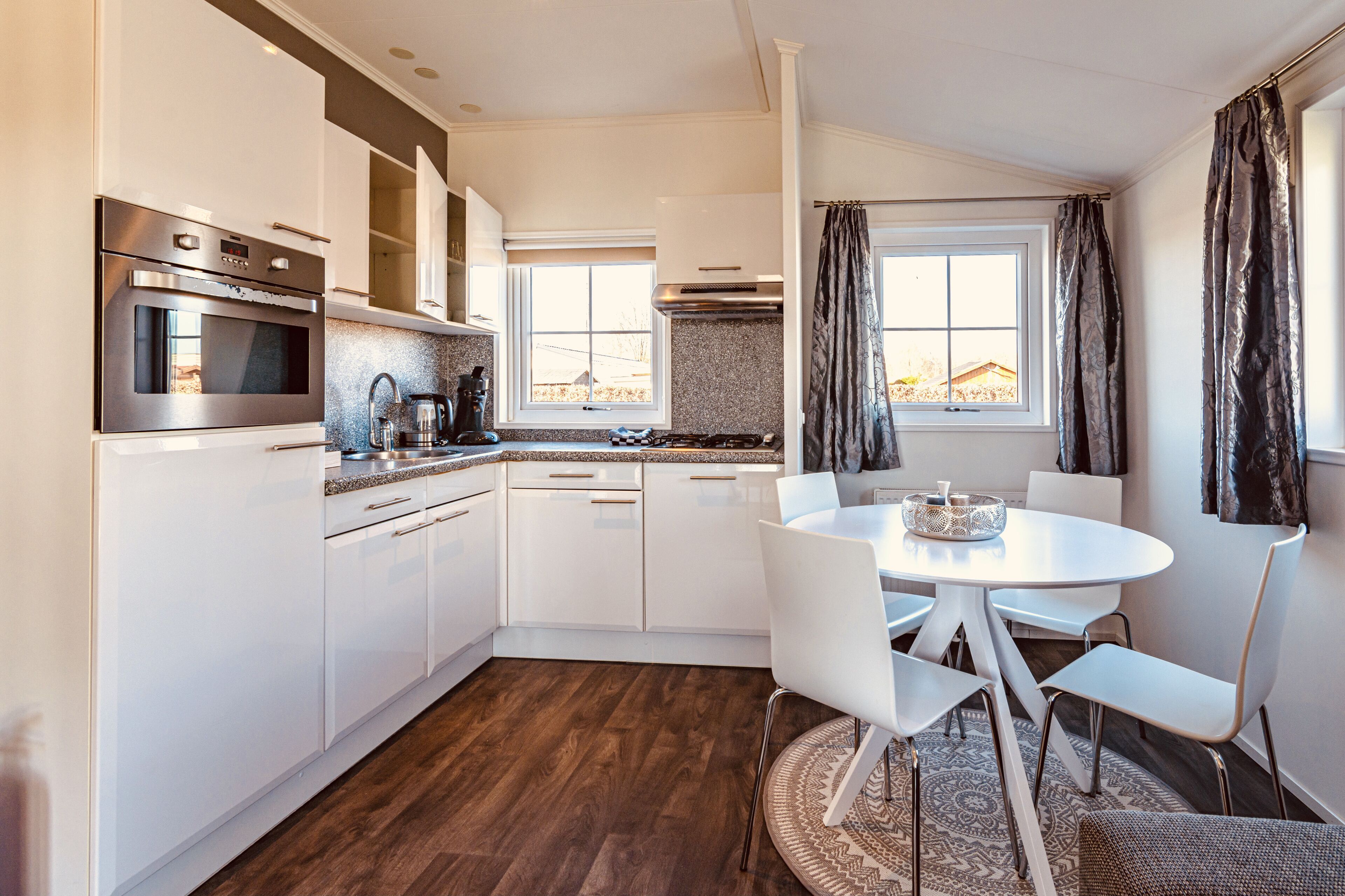 A modern kitchen with white cabinets, stainless steel appliances, and a dining area with white chairs and a round table.
