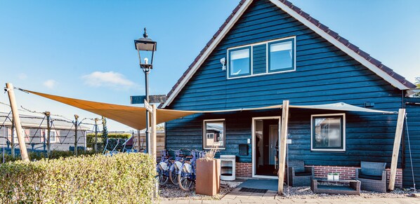 A blue wooden house with a triangular roof, a porch with a bench, and a bicycle rack. - Kroondomein Giethoorn (Giethoorn)