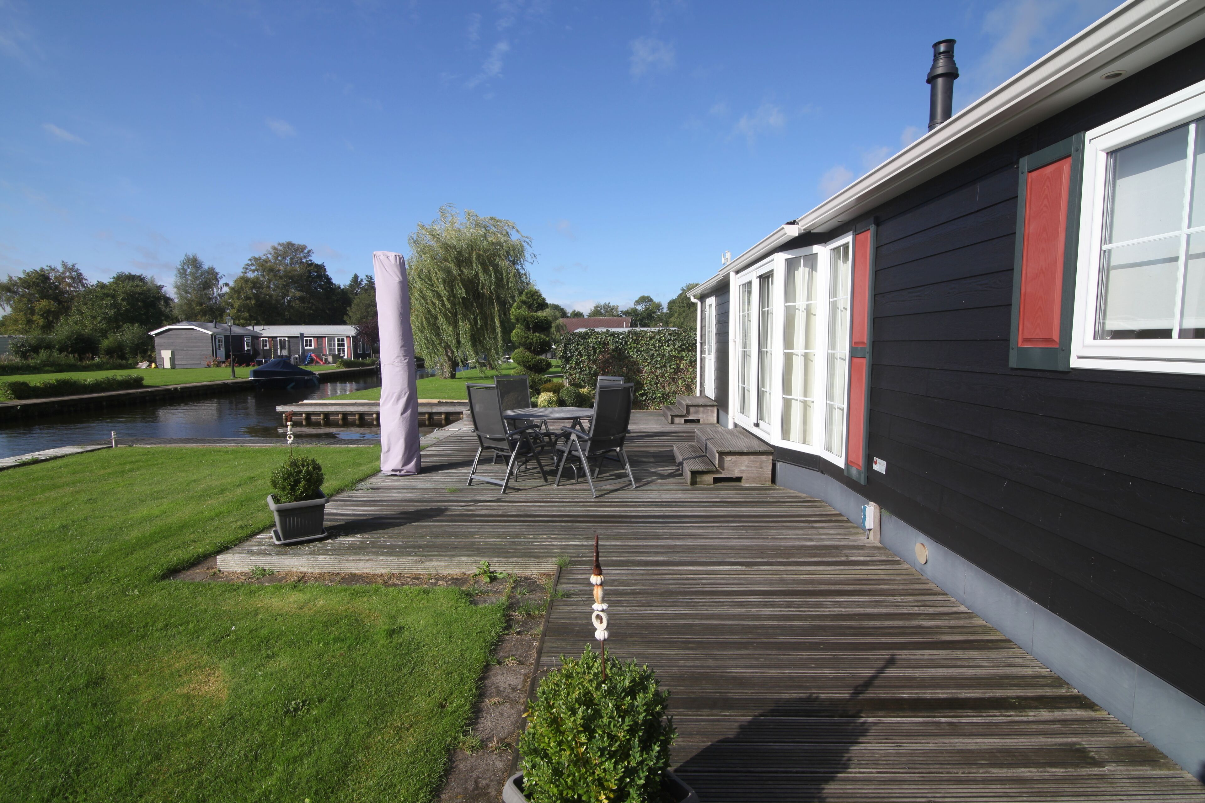 A wooden deck with outdoor furniture, a small garden, and a view of a water body and neighboring houses.