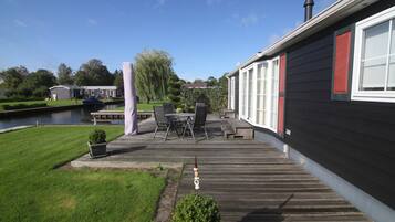 A wooden deck with outdoor furniture, a small garden, and a view of a water body and neighboring houses.