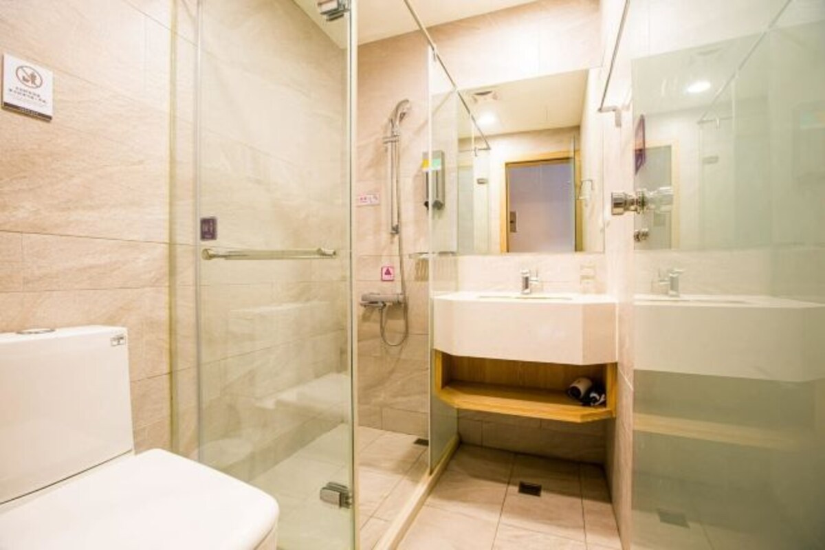 A modern bathroom with a glass-enclosed shower, a white toilet, and a sink with a wooden shelf.
