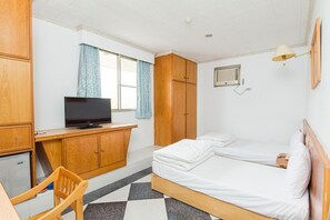 Una habitación de hotel con una cama, un escritorio con televisor, un armario y una ventana con cortinas.