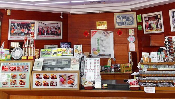 Un restaurante de varios niveles con mostrador de madera, diferentes productos alimenticios y un letrero sobre la escalera.