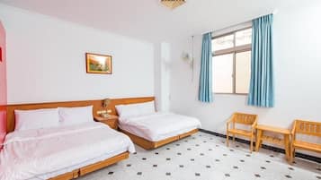 A hotel room with two single beds, a small table, two chairs, a window with curtains, and a picture on the wall.