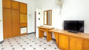Una habitación con un armario de madera, un escritorio con espejo, una televisión y un ventilador de pared.