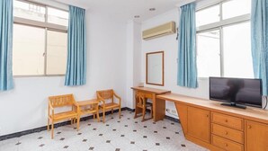 Una habitación con escritorio, dos sillas, televisor y espejo.