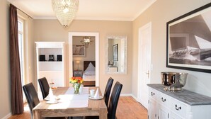 A dining room with a wooden table, black chairs, a chandelier, a white cabinet with drawers, and a framed picture on the wall. - 4-room apartment with balcony - Villa Park Ocean (Scharbeutz)