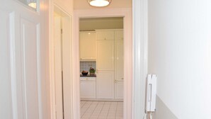 A narrow hallway leading to a kitchen with white cabinets and a white telephone on the wall. - 4-room apartment with balcony - Villa Park Ocean (Scharbeutz)