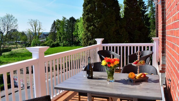 A wooden deck with a table and chairs, a white railing, and a brick wall. - 4-room apartment with balcony - Villa Park Ocean (Scharbeutz)