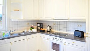 A kitchen with white cabinets, a built-in oven, a coffee maker, and a toaster. - 4-room apartment with balcony - Villa Park Ocean (Scharbeutz)