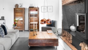 Ein modernes Wohnzimmer mit Couchtisch aus Holz, grauem Sofa und Kamin.