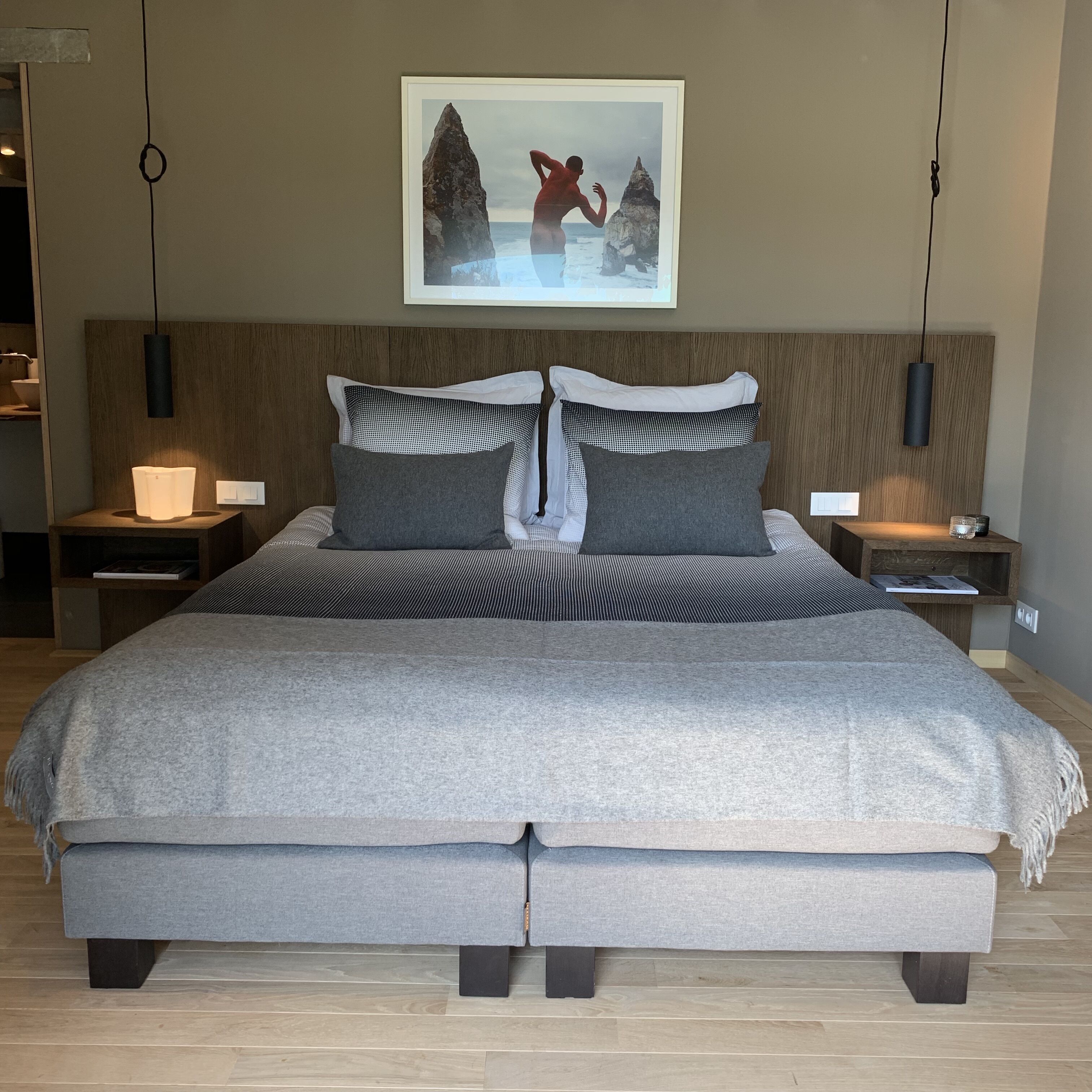 A modern bedroom with a large bed, two bedside tables, a wall-mounted artwork, and a hanging light fixture.