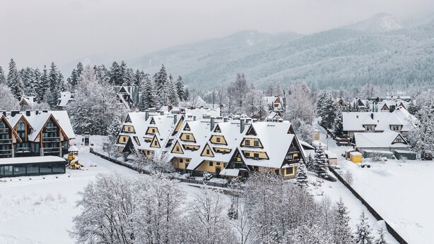 A snow-covered mountain village with chalet-style buildings, a ski lift, and a mountain backdrop. - Apartamenty Sun&Snow Kościelisko Chotarz (Koscielisko)
