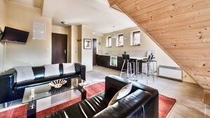 A modern living room with a black leather sofa, a glass coffee table, and a red rug. A kitchen with a bar area is visible in the background. - Apartamenty Sun&Snow Kościelisko Chotarz (Koscielisko)