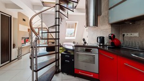 A modern kitchen with a stainless steel stove, red cabinets, and a spiral staircase. - Apartamenty Sun&Snow Kościelisko Chotarz (Koscielisko)
