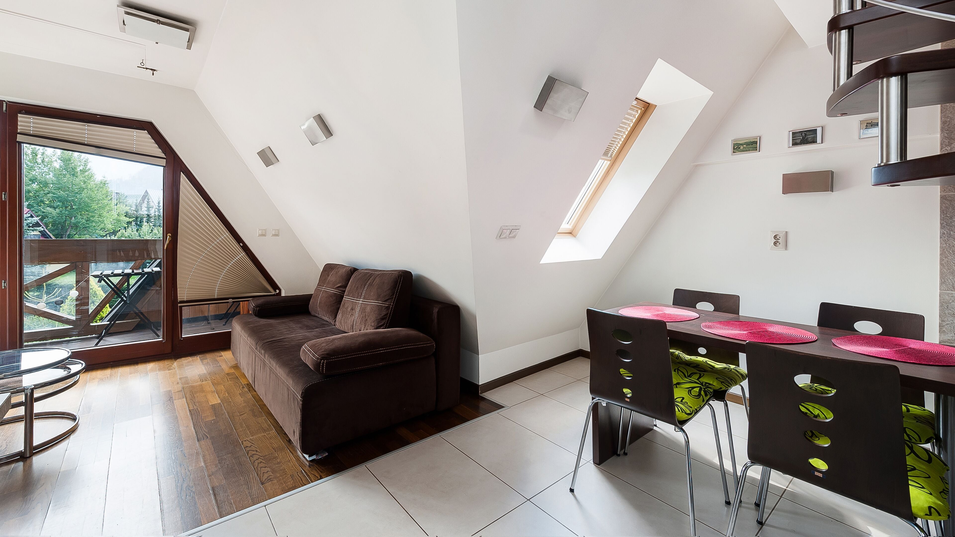 Een moderne woonkamer met een bruine bank, een eettafel met stoelen en een dakraam.