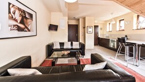 A modern living room with a black leather sofa, a glass coffee table, and a red rug. There is a kitchen area with a bar and stools, and a dining table. - Apartamenty Sun&Snow Kościelisko Chotarz (Koscielisko)