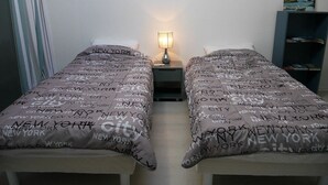 A hotel room with two beds, each with a grey bedspread featuring the text "New York City". There is a nightstand with a lamp between the beds, and a bookshelf to the right. - Apartment with terrace, parking and port view in Capbreton (Capbreton)