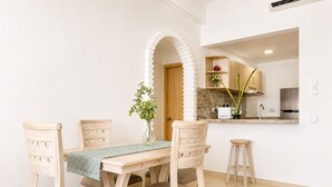 Un coin repas avec une table et des chaises en bois, un vase agrémenté de verdure, et une cuisine en arrière-plan.